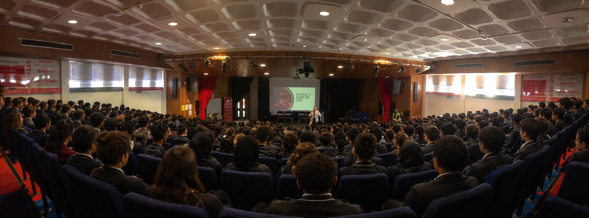 Edited photograph of Mark Stevens speaking at a school assembly, with additional audience members added
